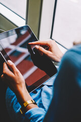 Cropped back view of young woman choosing music application on website touching with finger on display of modern touch pad connected to public transport wifi.Female passenger with tablet in hands