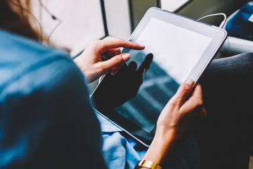 Cropped back view of young woman holding modern tablet in hands and touching with finger on display...