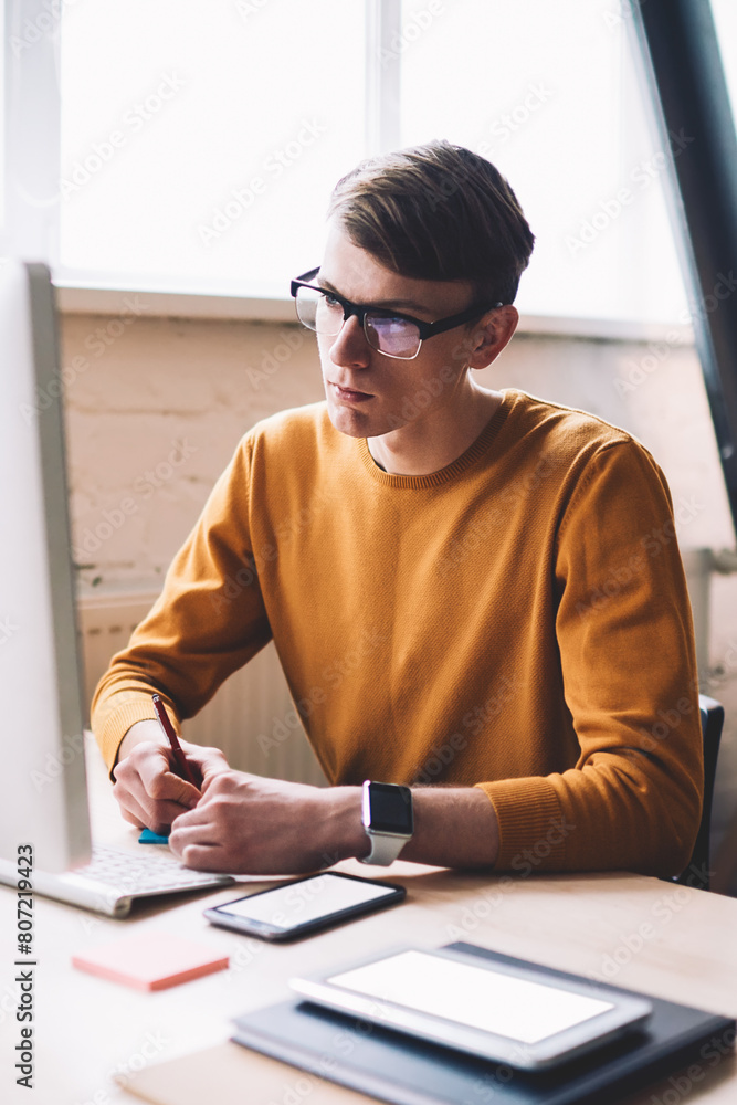 Poster young hipster guy in spectacles watching important webinar on web page internet via modern computer 