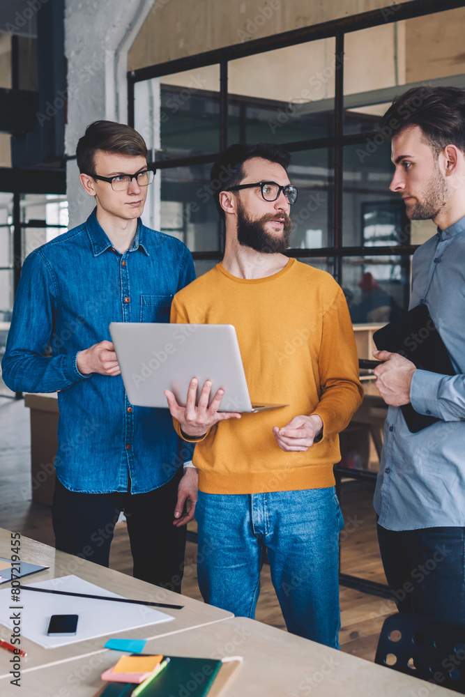 Poster caucasian male employees discussing ideas for solution using laptop computer for searching informati