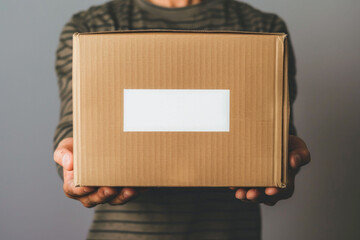 Close-up cardboard box with a blank white sticker on it in the male hands. AI generative