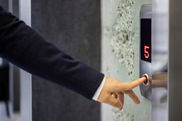 A professional businessman in a dark suit pressing an elevator button, symbolizing convenience and...