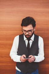 Young caucasian hipster guy in fashionable waistcoat chatting with followers in social networks using modern smartphone device and wireless internet near copy space area for advertising text