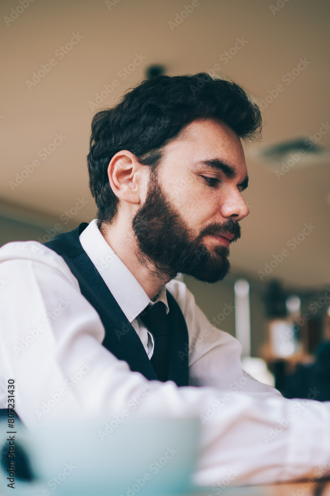 Poster serious bearded man searching information in internet web page on cellphone while sitting at table i