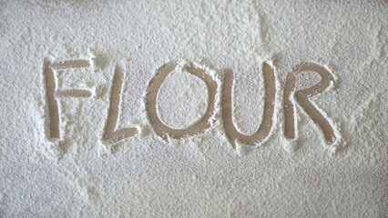 Flour written on wooden table with finger over dusted flour - Powered by Adobe