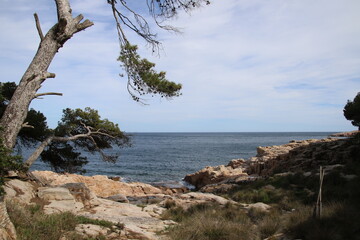 Natural and small coves of the Costa Brava with boats in the background and the blue sky with clouds and blue water. A beautiful place for vacations.