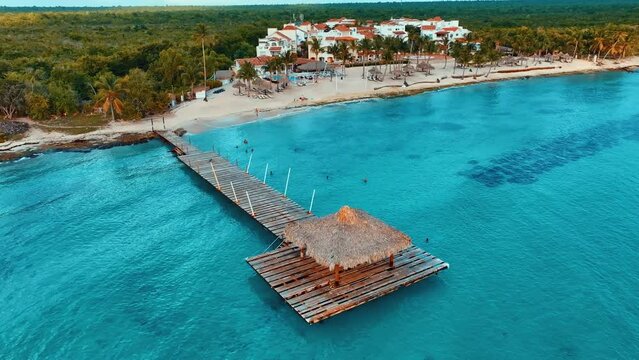 A wooden jetty over open water off a Caribbean beach. Texture of blue transparent sea water. Thatched roof on a wooden house. Travel and recreation. Aerial drone shot of blue water.