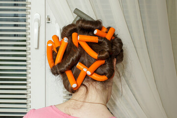 Orange and gray hair curlers for hair on the head of a young woman. Creating a hairstyle at home.