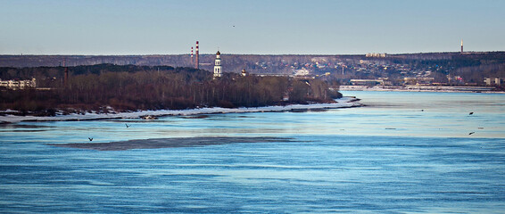Winter city landscape. Panorama. On the nearest bank of a wide river, in a grove there is an...