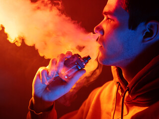 A man exhales steam from an electonic cigarette. Pod in hand