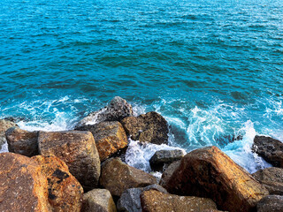 The blue ocean waves hit the rocks hard on the beach. Seaspray splashes into the sky in the...