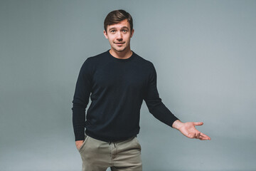 A young man in a blue sweater on a gray background. The man makes a hand gesture, inviting you to...