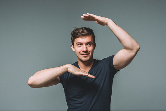 Waist portrait of a young handsome man with a muscular build on a gray background. A man dances, depicts a tectonic dance or waacking dance with his hands
