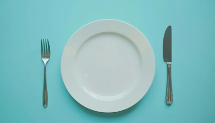 Top view of a chic table arrangement with an unoccupied white plate cutlery on a blue backdrop