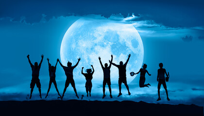 Group of friends jumping on top of dune with arms raised in air with full blue moon 