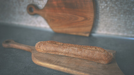 A baguette of dark bread on a wooden cutting board. Close-up 6K