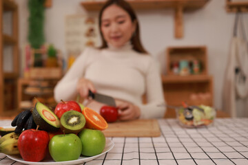 Indulging in a wide range of fresh fruits and vegetables, a healthy, pregnant Asian woman sits back on her comfortable home sofa, radiating a sense of calm and well-being.