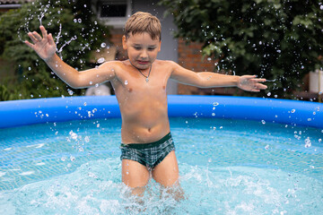 Boy child plays in the pool in summer. The child jumps out of the water in a large amount of...