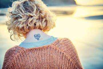 Back view of a young blonde woman with a tattoo in is nape in a beach.