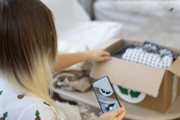 Having put old clothes in a box, a woman takes a photo of it on her phone so that she can post an advertisement for sale on the Internet. Sorting clothes and selling them online. Recycling clothing.