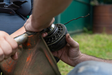 Replacing the nylon thread on a grass trimmer. A man unscrews the nut to change the line on the...