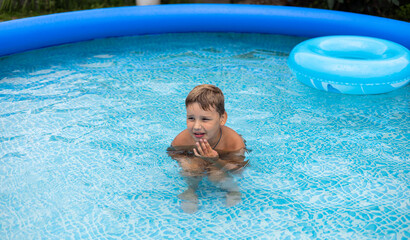 A pensive child sits in the water in a swimming pool in summer. A child sitting in the pool is thinking about something and looking to the side. The concept of spending summer time in the pool.