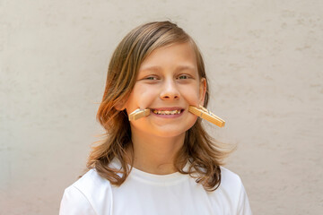 Portrait of a long-haired boy of 11 with a stretched out clothespin smile on a light colored...