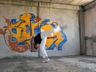A guy in white sweatpants does an acrobatic Bedouin somersault against the backdrop of beautiful graffiti