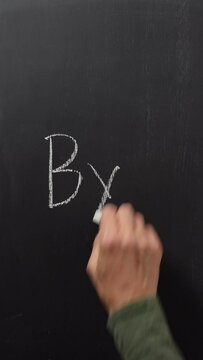 A hand writes the word bye with white chalk on a black board. Vertical video