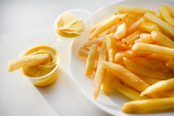 French fries on a white plate with sauce. Delicious fried crispy potatoes.