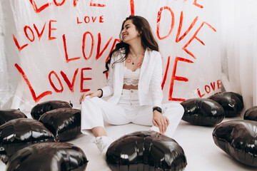 Woman sitting with kisses lipstick near black foil balloons, the word LOVE hand-painted on plain...