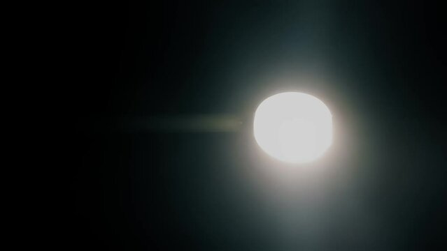 In the dead of night, a defective lamppost flickers ominously, its haunting glow revealing secrets in the shadows. Vertical handheld close-up shot.
