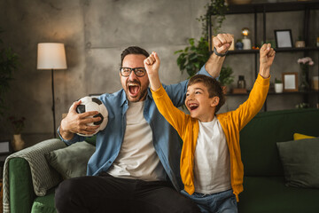 Father and son watch football match and cheer at home