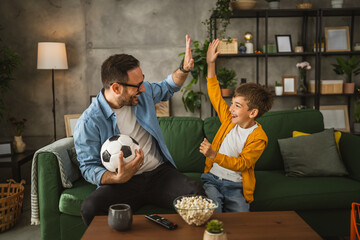 Father and son watch football match and cheer at home