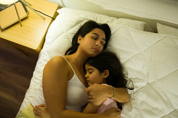 Tranquil latin mother and her daughter asleep together in a warm home bedroom at night