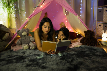 Mother and daughter bonding over reading in a diy tent with fairy lights, creating a cozy evening ambiance at home