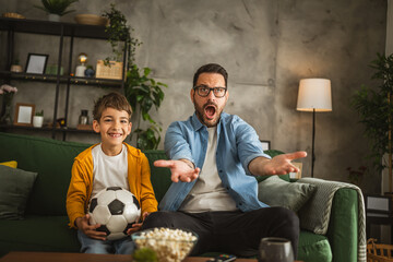 Father and son watch football match and cheer at home