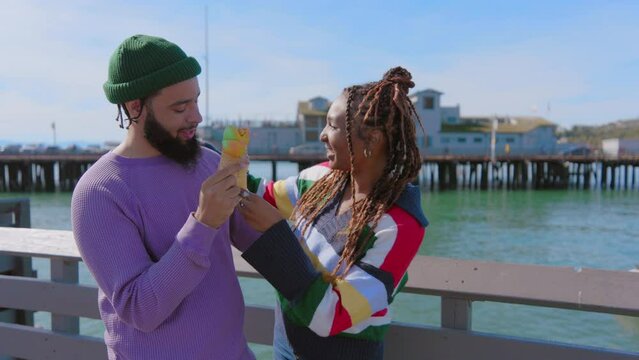 Charismatic young African American couple having a romantic date on a pier in Santa Barbara, bearded black man in green beanie hat licking ice-cream cone of his beloved. High quality 4k footage