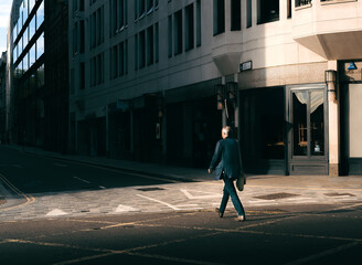 Street Photo of Man Walking Across the Road in Shaft of Golden Sunlight and Dark Shadows in London,...