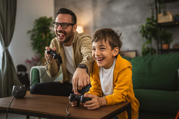 Father and son play video games with joystick and have fun at home