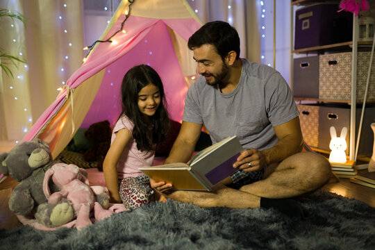 Dad and daughter cozy up in a homemade tent with lights, reading a storybook and creating a warm nighttime ambiance - Powered by Adobe