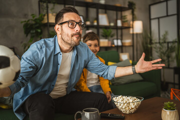 Father and son watch football match and cheer at home