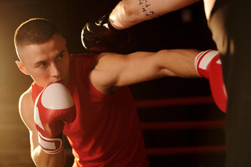 Young strong man in red boxing gloves looking at his rival and kicking him on chest while...