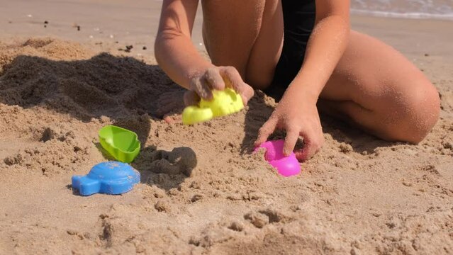 Little girl playing with molds in sand at the beach, enjoying summer vacation with family