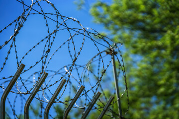 Barbed wire security tape against a blue sky with trees
