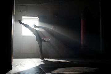 Backlit silhouette of young male athlete in sportswear standing on the floor of training hall and...