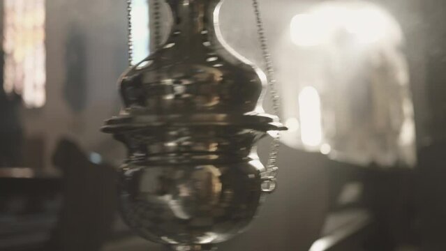 Christian metal thurible swinging on chains in church close up. Religious censer in smoke closeup. Incense burning during worship ritual in cathedral