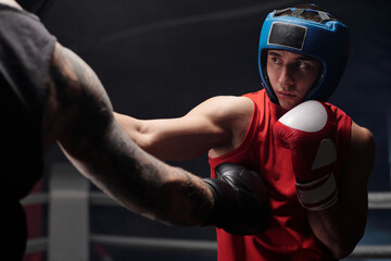 Hand in black boxing glove of muscular brutal athlete with tattoos kicking his rival in red...
