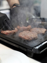 chef con guantes negros friendo carne de hamburguesas a la plancha