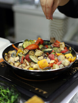 chef echando sal a la sart&eacute;n con verduras y vegetales cocin&aacute;ndose en el fuego de la cocina